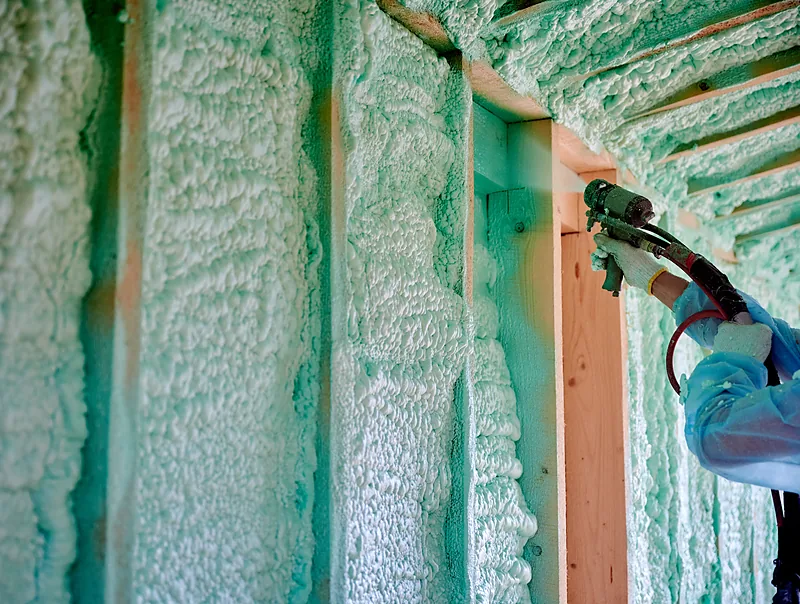 Spraying foam into wall bays beside a framed window opening
